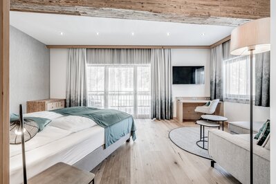 Modernes Hotelzimmer mit Bett, Sitzecke und großen Fenstern im Hotel Jenewein.