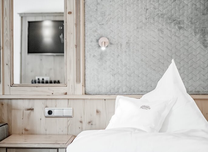Ein helles Studio mit weiß bezogenem Bett, Holzverkleidung und Spiegel im Hotel Jenewein.
