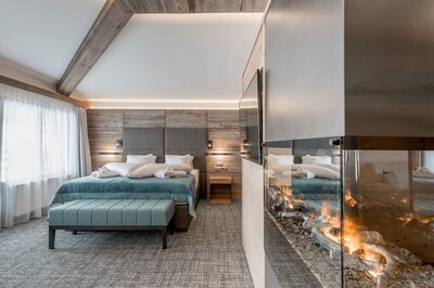 Ein modernes Hotelzimmer mit Doppelbett, Holzverkleidung und offenem Kamin.