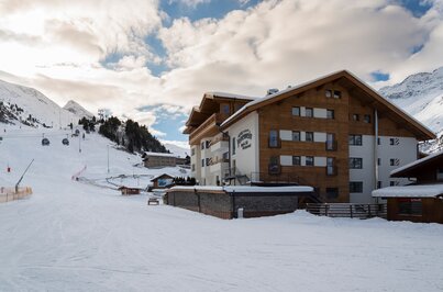 Das Hotel Jenewein liegt direkt an der Skipiste in Obergurgl vor verschneiten Bergen.