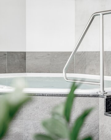 Ein Whirlpool mit Edelstahlhandlauf in einem hellen Wellnessbereich.