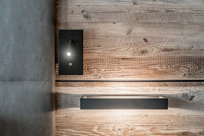 Eine moderne Wandlampe leuchtet an einer rustikalen Holzwand neben einer gepolsterten Wandverkleidung.