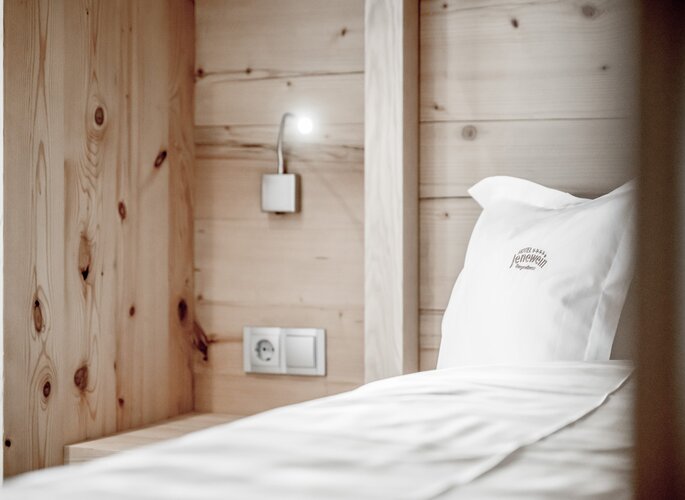 Holzverkleidetes Bett im Hotel Jenewein Ein Bett mit weißer Bettwäsche und Kissen vor einer Holzverkleidung im Hotel Jenewein.