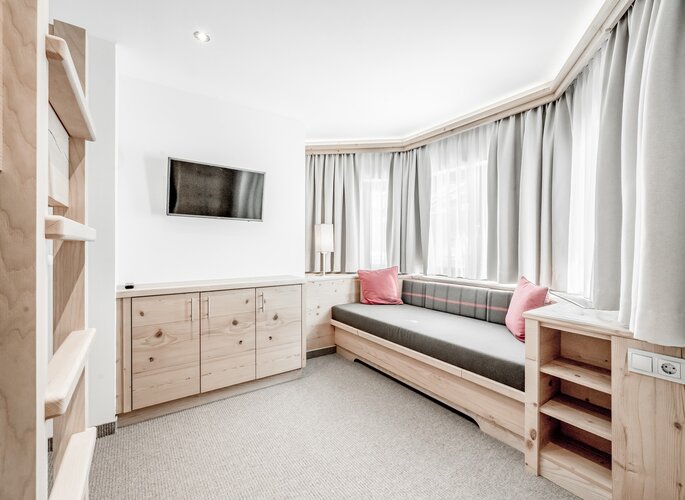 Turmsuite mit Kinderschlafzimmer im Hotel Jenewein Ein separates Kinderschlafzimmer mit Sitzbank, TV und hellem Holzmobiliar in der Turmsuite.