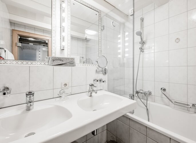 Helles Badezimmer mit Waschbecken, Badewanne und Dusche im Hotel Jenewein.