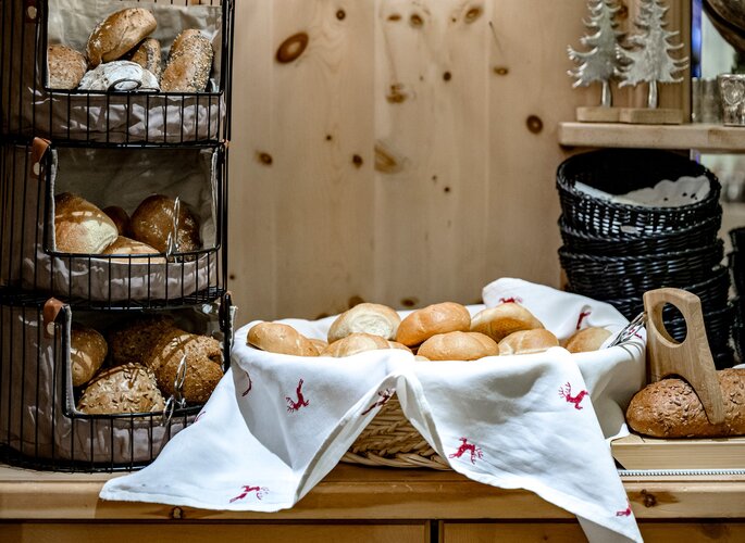 Verschiedene Brötchen und Brote stehen in Körben auf einem Frühstücksbuffet.