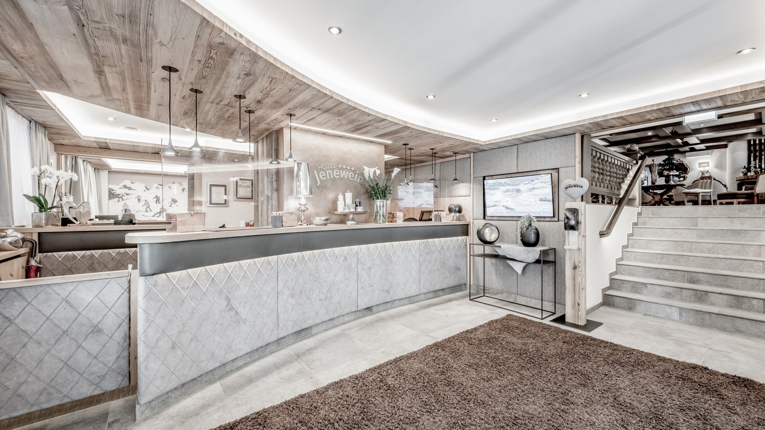 Die helle Rezeption des Hotel Jenewein mit Holzdecke, Empfangstresen und Treppe.