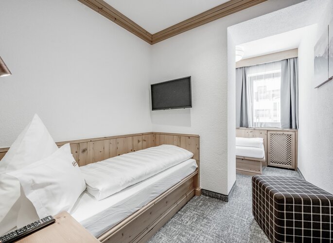 Ein helles Studio mit Einzelbetten, kleinem TV und Sitzbank, geeignet für Familien.