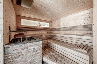 Eine holzverkleidete Sauna mit Sitzbänken und Ofen im Wellnessbereich.