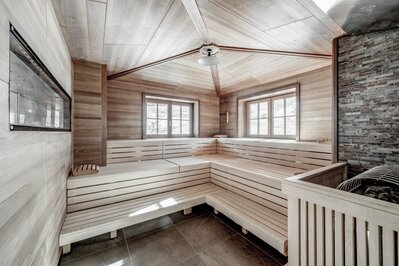 Eine helle Sauna mit Holzsitzen und Blick auf die verschneite Berglandschaft.