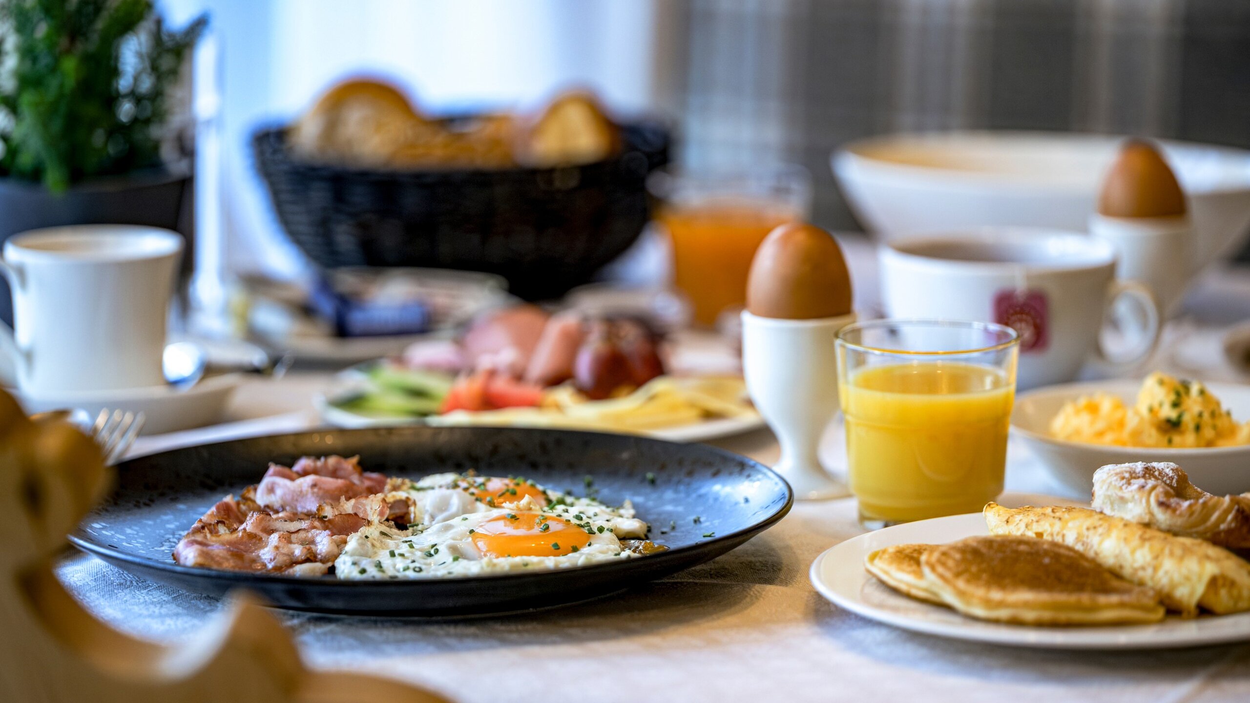 Ein gedeckter Frühstückstisch mit Eiern, Brot, Saft und weiteren Frühstücksspeisen.