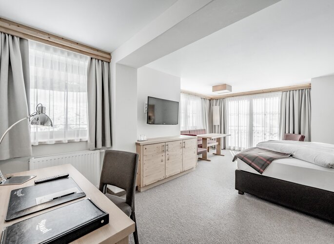 Turmsuite mit Bergblick im Hotel Jenewein Helle Turmsuite mit Bett, Sitzecke und großen Fenstern mit Blick auf die Berge.