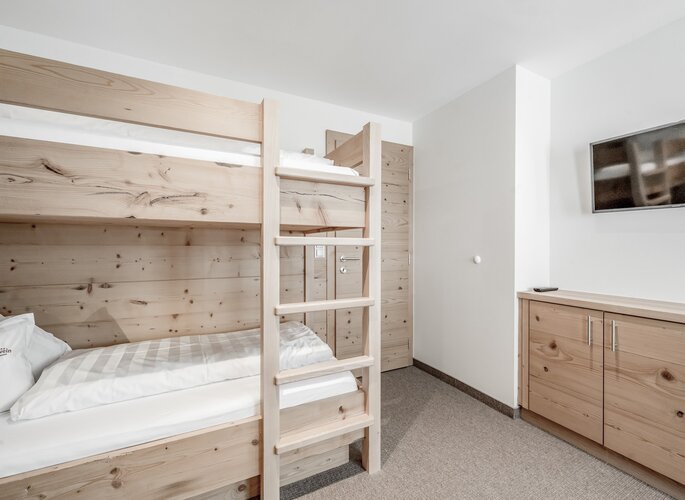 Turmsuite mit Etagenbett im Hotel Jenewein Ein helles Kinderzimmer mit Holzetagenbett, Kleiderschrank und Wandfernseher in der Turmsuite.