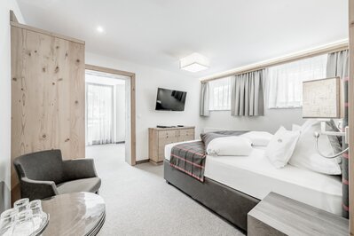 Helles Hotelzimmer mit Doppelbett, Sessel, TV und Holzmöbeln im Hotel Jenewein.