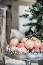 Eine dekorative Früchteplatte mit Äpfeln und Zitrusfrüchten steht vor einem Weihnachtsbaum.