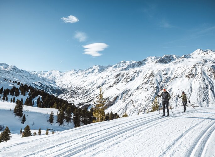 Zwei Langläufer auf einer gespurten Loipe mit Blick auf die verschneiten Berge in Obergurgl.