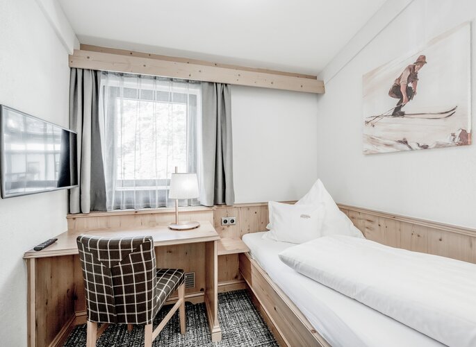 Ein kleines Studio mit Einzelbett, Schreibtisch, Fenster und TV im Hotel Jenewein.