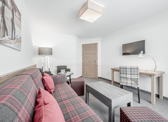 Familienzimmer im Hotel Jenewein in Obergurgl Heller Wohnbereich im Familienzimmer mit Sofa, Schreibtisch, TV und Holztür.