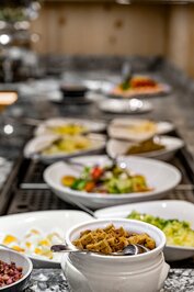 Im Hotelrestaurant stehen verschiedene Buffetgerichte und Salate in Schalen auf einer Anrichte.