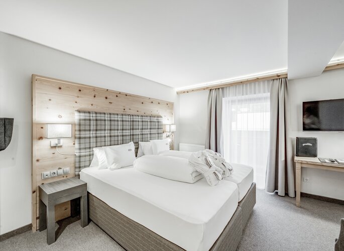 Ein helles Zirbenzimmer mit Doppelbett, Holzkopfteil und Fenster im Hotel Jenewein.