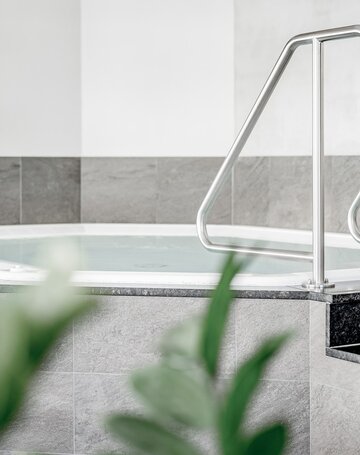 Ein Whirlpool mit Edelstahlhandlauf und hell gefliester Umrandung im Wellnessbereich.