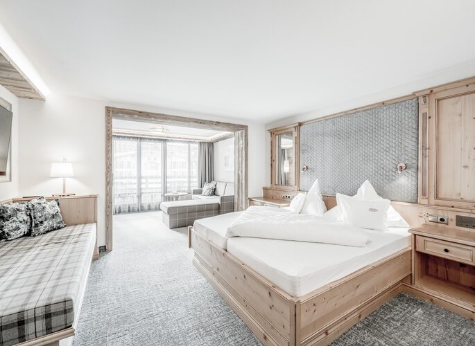 Die Juniorsuite im Hotel Jenewein zeigt ein helles Schlafzimmer mit Sitzecke und viel Holz.