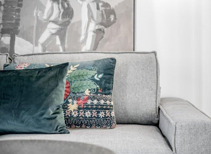 Komfortzimmer im Hotel Jenewein in Obergurgl Ein graues Sofa mit dekorativen Kissen vor einem Wandbild im Komfortzimmer des Hotel Jenewein.