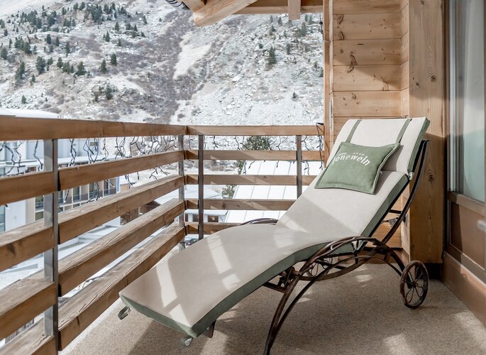Balkonliege mit Bergblick im Hotel Jenewein Auf dem Balkon steht eine Liege mit Kissen und Blick auf die verschneite Berglandschaft.