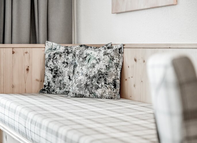 Doppelzimmer im Hotel Jenewein mit Holzbett Ein schlichtes Doppelbett mit Holzbettverkleidung, gemustertem Bezug und dekorativen Kissen im Hotelzimmer.