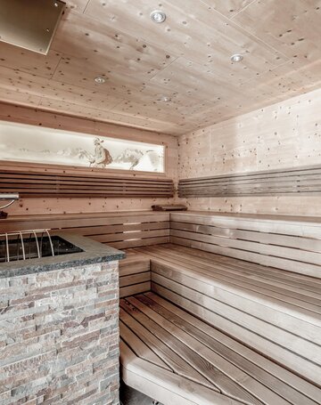 Eine holzverkleidete Sauna mit Sitzbank und Steinofen im Wellnessbereich.