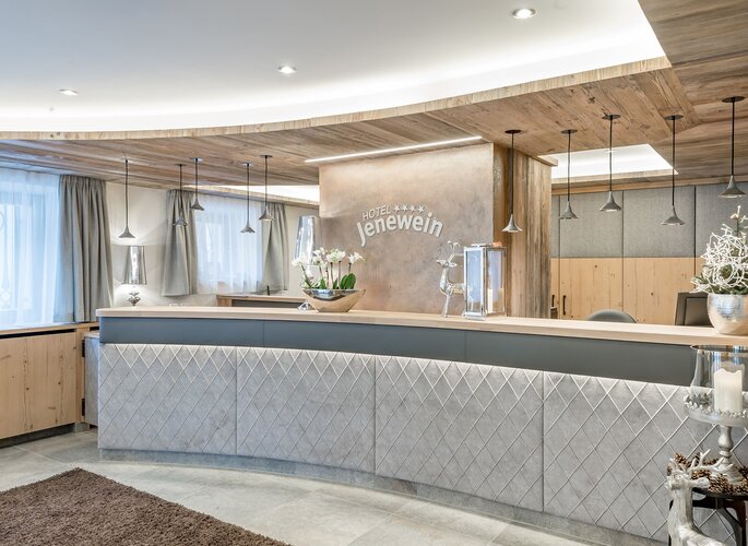 Die helle Rezeption im Hotel Jenewein mit Holzdecke und modernen Lampen.