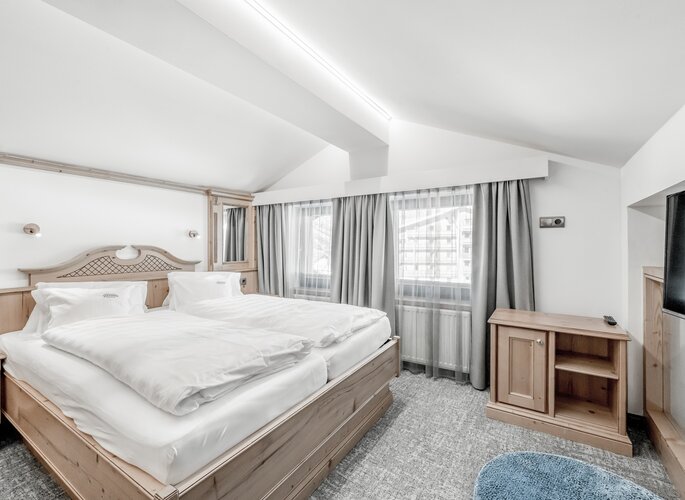 Helles Maisonettenzimmer mit Doppelbett, Holzmöbeln und großen Fenstern im Hotel Jenewein.