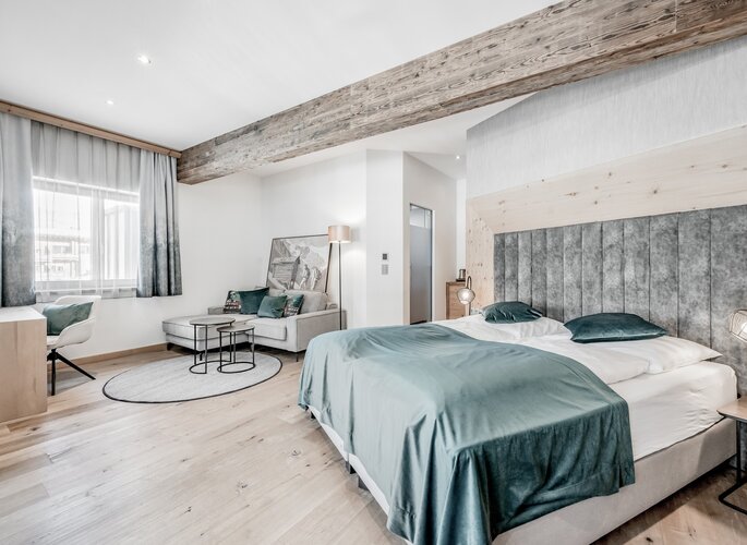 Helles Komfortzimmer mit Doppelbett, Sitzecke und sichtbaren Holzbalken im Hotel Jenewein in Obergurgl.