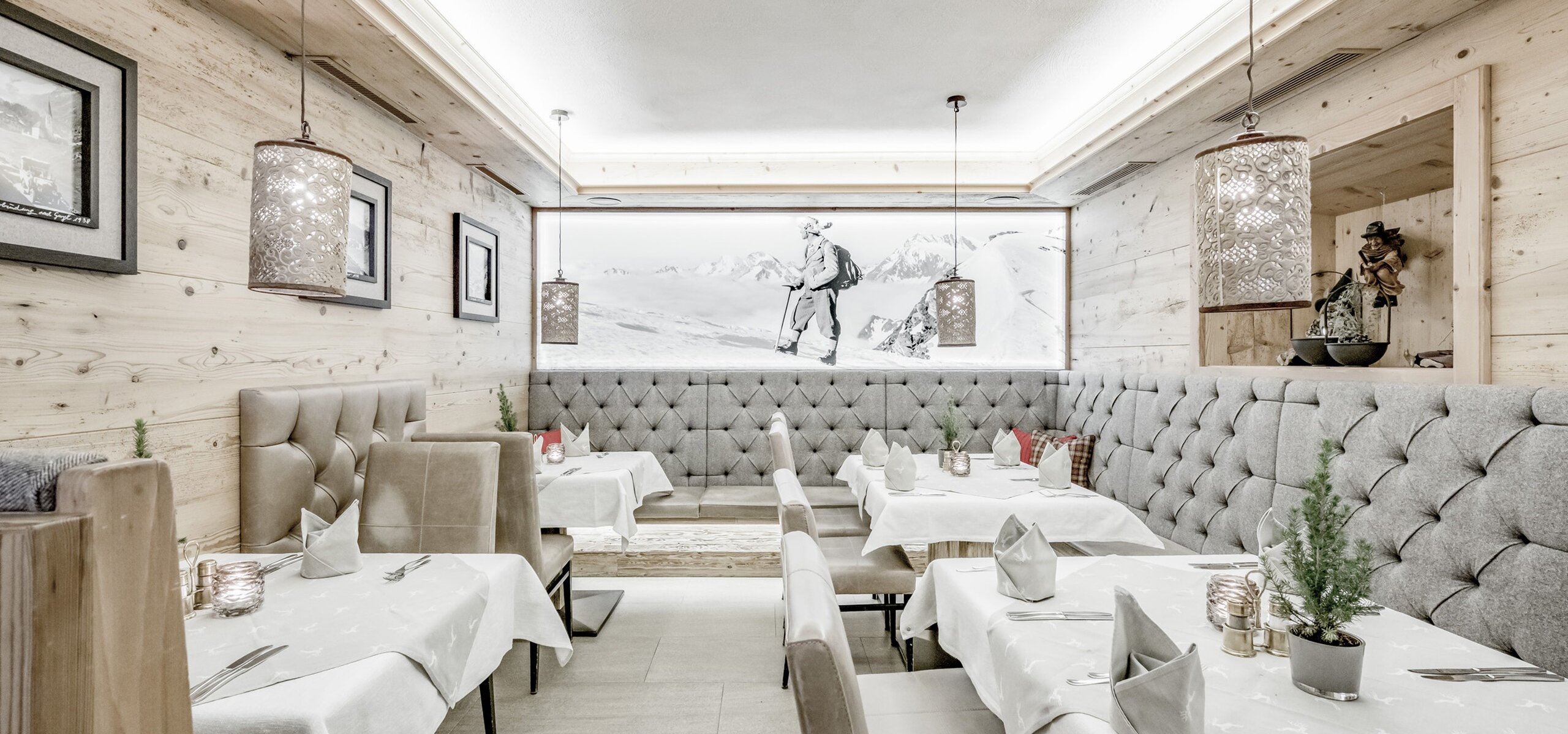 Ein stilvoll gedecktes Hotelrestaurant mit hellen Holzwänden, gepolsterten Bänken und Bergmotiv an der Wand.