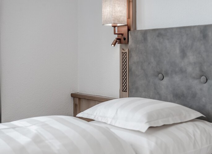 Appartement in Obergurgl: Bett mit gepolstertem Kopfteil Ein Bett mit weißer Bettwäsche, gepolstertem Kopfteil und Wandlampe in einem hellen Appartement.