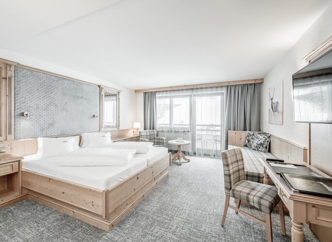 Helles Doppelzimmer mit Holzmöbeln, zwei Betten und Sitzbereich vor dem Balkon.