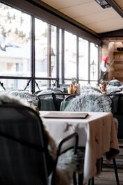 Im Restaurant des Hotel Jenewein stehen gedeckte Tische mit Blick auf die verschneite Bergkulisse.