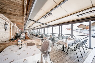 Ein helles Restaurant mit Holzakzenten und großen Fenstern blickt auf die verschneite Skipiste.