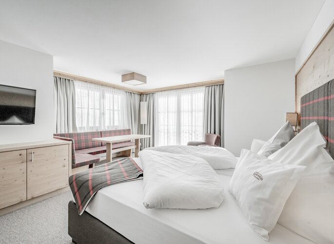 Helles Hotelzimmer mit Bett, Sitzbank und großen Fenstern im Hotel Jenewein.