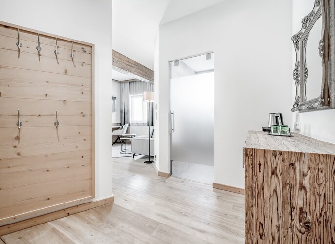 Komfortzimmer mit Holzdetails im Hotel Jenewein Der helle Eingangsbereich eines Komfortzimmers mit Holzdetails, Garderobe und Blick in den Wohnbereich.