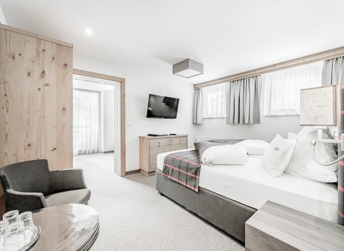 Helles Familienzimmer mit Doppelbett, Sitzecke, Fernseher und Holzmöbeln.