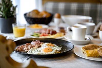 Ein Frühstückstisch mit Eiern, Speck, Brot, Saft und Kaffee im Hotelrestaurant.