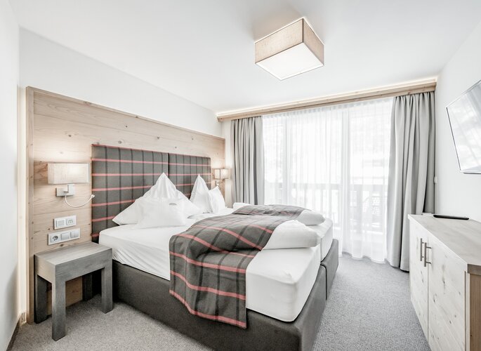 Helles Familienzimmer mit Doppelbett, Holzdetails und großem Fenster im Hotel Jenewein.