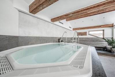 Ein heller Whirlpool im Wellnessbereich mit Holzdeckenbalken und Liegebereich.