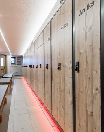 Holzschränke im Skidepot des Hotel Jenewein mit Sitzbänken entlang des Gangs.