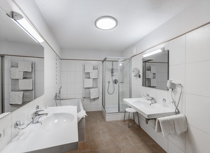 Familienappartement: modernes Bad im Landhaus Jenewein Helles Badezimmer mit Doppelwaschbecken, Dusche, Badewanne und Handtüchern im Familienappartement.