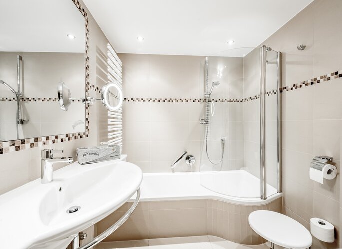 Badezimmer mit Dusche in der Juniorsuite Modernes Badezimmer mit Dusche, Waschbecken, Badewanne und weiß-beigen Fliesen in der Juniorsuite.