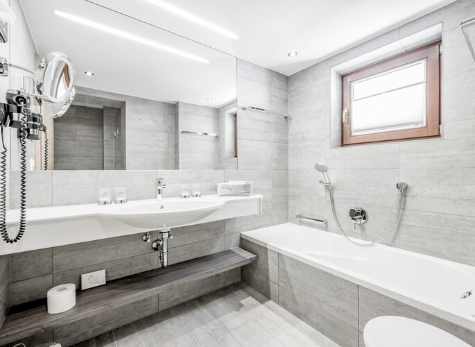 Modernes Badezimmer der Turmsuite im Hotel Jenewein Modernes Badezimmer mit Badewanne, Waschtisch und großer Spiegelwand in der Turmsuite.