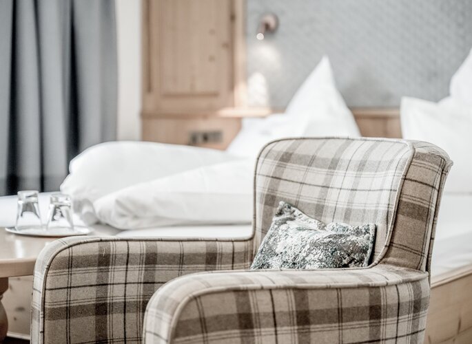 Doppelzimmer im Hotel Jenewein in Obergurgl Ein gemütliches Doppelzimmer im Hotel Jenewein mit kariertem Sessel, hellem Bett und klassischem Ambiente.