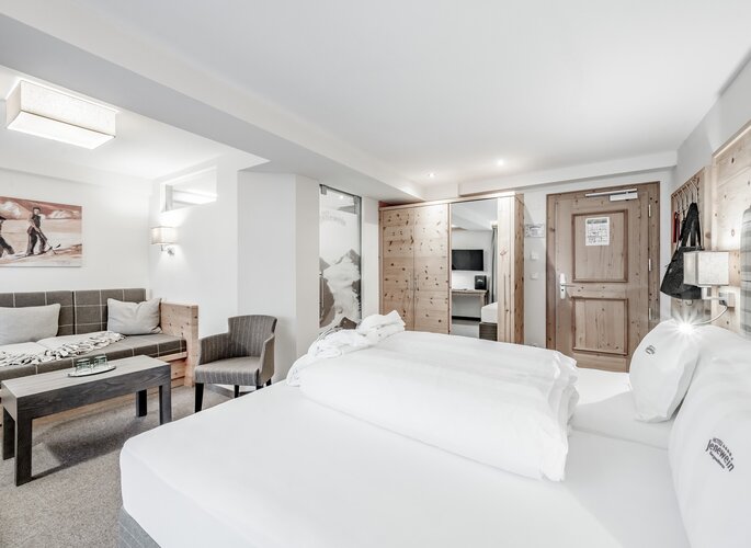 Ein helles Zirbenzimmer mit Doppelbett, Sitzecke und Holzmöbeln im Hotel Jenewein.